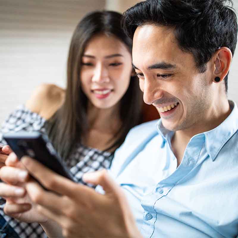 Man with a bluetooth hearing aid watching a video on his phone with his wife.