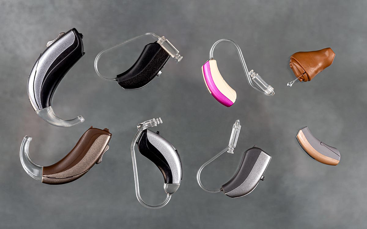 Eight different hearing aids in various colors and shapes are arranged on a gray background, showcasing a variety of styles and designs.