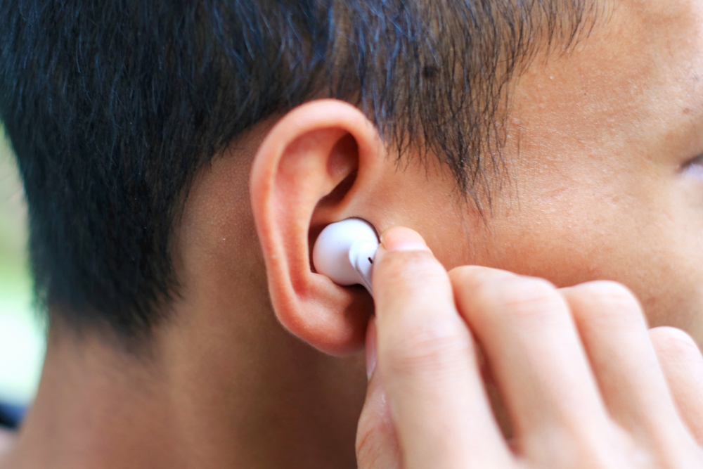 A person inserting a white wireless earbud into their ear, shown in a close-up focusing on the side of their head and hand.