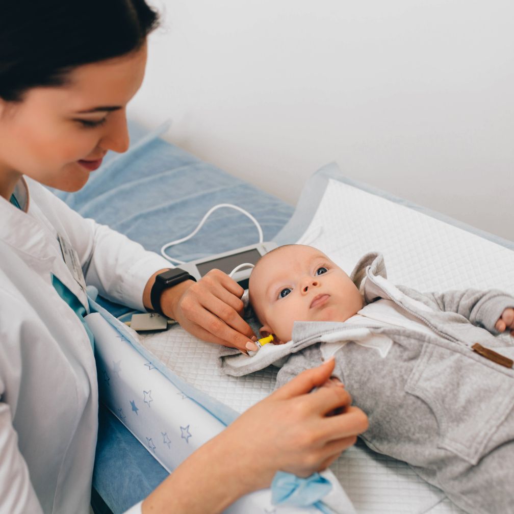 A healthcare worker checks a babys hearing using medical equipment while the baby lies on an examination table.